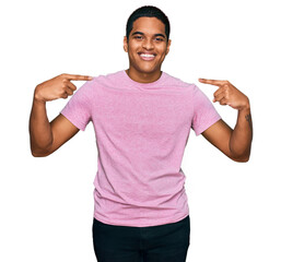 Young handsome hispanic man wearing casual pink t shirt looking confident with smile on face, pointing oneself with fingers proud and happy.