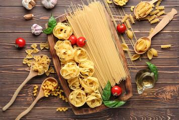 Composition with different uncooked pasta, spices and tomatoes on wooden background - obrazy, fototapety, plakaty