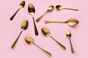 Different golden spoons on pink background
