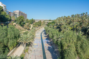 Fototapeta na wymiar View of the gardens of the Vinalopo riverbed with palm trees and residential buildings in central Elche, Alicante, Spain