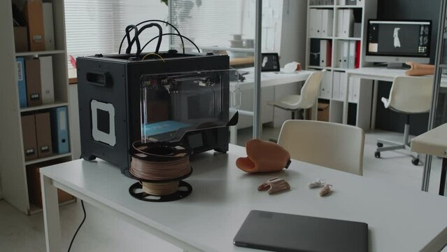 3D printing machine with prototypes of prosthetics and light-weighted material like carbon fiber, titanium and aluminum lying on table of laboratory