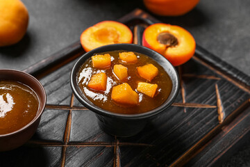 Board with bowl of sweet apricot jam on black background