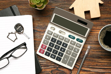 Calculator, wooden house, keys, cup of coffee, eyeglasses and houseplant on wooden background....
