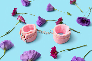 Pink handcuffs from sex shop and beautiful flowers on blue background, closeup
