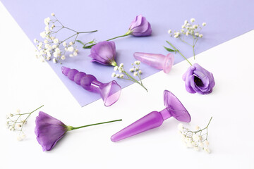 Anal plugs from sex shop and beautiful flowers on color background