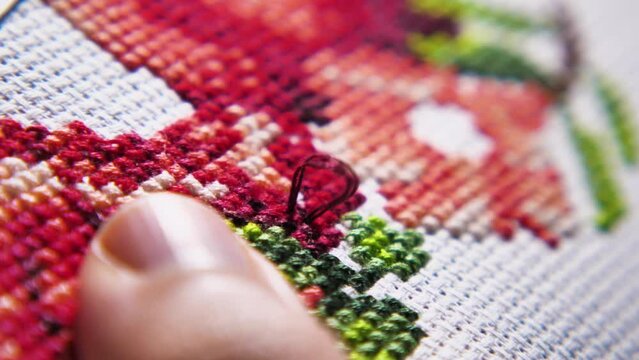 Part of the working process over a beautiful cross stitch embroidery. Slow motion shooting. Close-up of a woman's fingers busy with embroidery. A woman's hobby. The concept of needlework