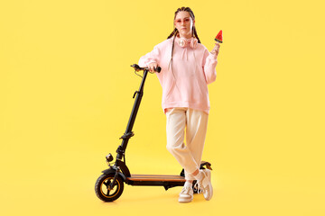 Young woman with lollipop and electric scooter on yellow background