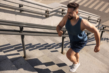 Smiling man running up stairs outdoors on sunny day. Space for text