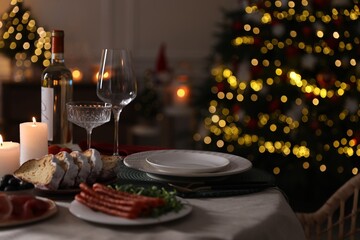 Fototapeta na wymiar Christmas table setting with burning candles, appetizers and dishware indoors