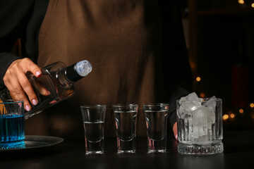 Female bartender with shots of cold vodka on table in bar