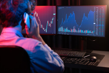 Young investor stock trader calling with broker to invest earning highest profit on current market graph online in real time at neon light modern office, monitor showing investment exchange. Gusher.