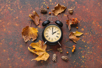 Alarm clock with viburnum and autumn leaves on grunge background