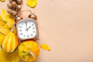 Alarm clock with pumpkins, acorns and autumn leaves on beige background