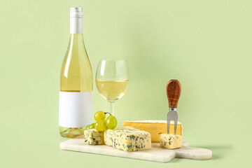 Board with tasty cheese, grapes, bottle and glass of wine on green background