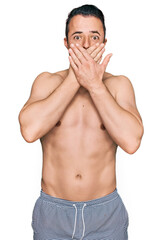Fototapeta premium Handsome young man wearing swimwear shirtless shocked covering mouth with hands for mistake. secret concept.