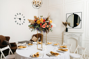 Elegant Dining Table Setup in Modern Event Space. A beautifully arranged dining table with a floral centerpiece in a chic event space with modern decor and a striking wall clock.
