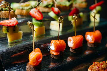 assortment of canapés on skewers on a glass stand on a catering table.