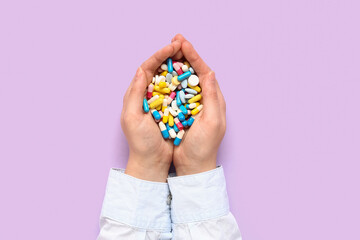 Female hands with many different pills on lilac background