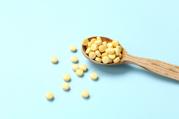Wooden spoon with yellow pills on blue background