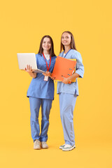 Female medical students with laptop and folders on yellow background