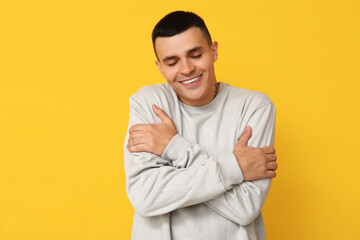 Handsome young man hugging himself on yellow background