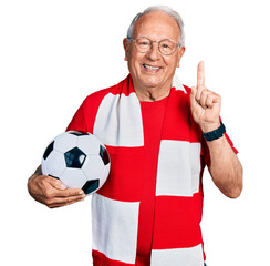 Senior man with grey hair football hooligan holding ball with a big smile on face, pointing with...