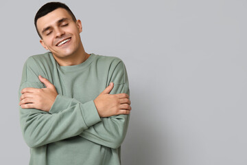 Handsome young man hugging himself on grey background