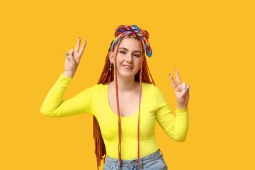 Obraz na płótnie Canvas Portrait of pretty young woman with dreadlocks showing victory gestures on yellow background