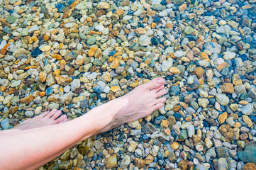 Beautiful female legs in the water of a lake with stones