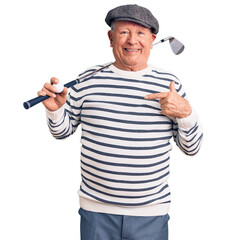 Senior handsome grey-haired man holding golf club and ball pointing finger to one self smiling...