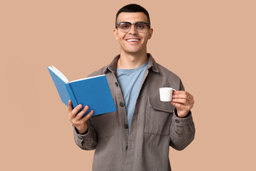 Handsome young man reading book and drinking coffee on beige background