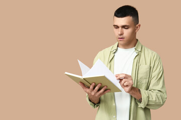 Handsome young man reading book on beige background