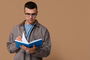 Handsome young man reading book on beige background