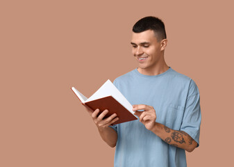 Handsome young man reading book on beige background