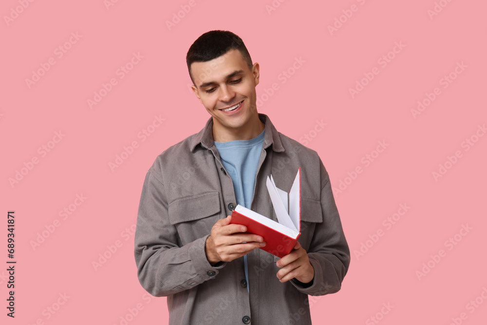 Poster Handsome young man reading book on pink background