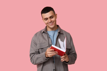 Handsome young man reading book on pink background