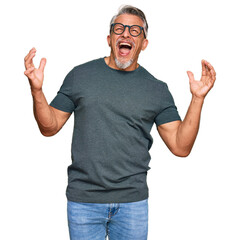 Fototapeta premium Middle age grey-haired man wearing casual clothes and glasses crazy and mad shouting and yelling with aggressive expression and arms raised. frustration concept.