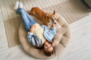 Little girl with cute Corgi dog lying at home, top view