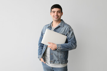 Happy young man with laptop on light background
