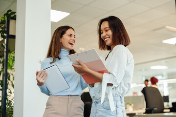 Diverse business woman chatting in an office while using tablet and a clipboard