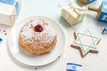 Plate with tasty donut, gifts and decor for Hanukkah celebration on light background