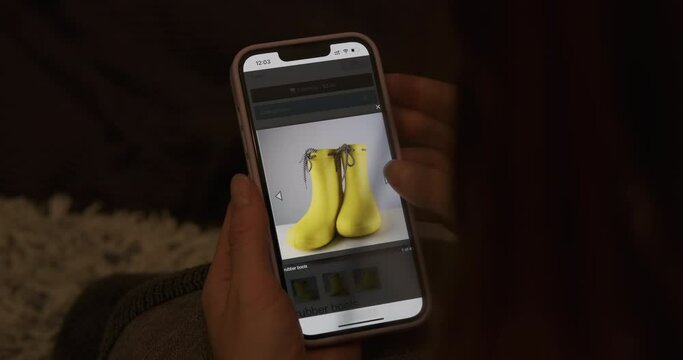 View product photo in detail on smartphone screen. Rubber yellow boots. Website, online shopping. Woman choosing shoes before buying.
