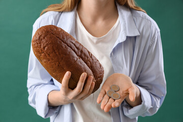 Young woman with bread and coins on green background, closeup. Price rise concept