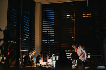 A cross generational corporate team working late, analyzing reports, and collaborating to achieve business growth and meet project deadlines.