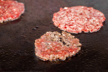 Burger minced beef patty frying with oil on baking sheet, close-up, selective focus