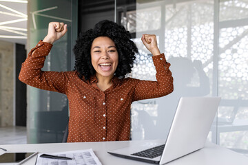 Happy female businesswoman joyfully raising her hands up in the office, African American woman got...