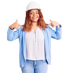 Young latin woman wearing architect hardhat looking confident with smile on face, pointing oneself with fingers proud and happy.