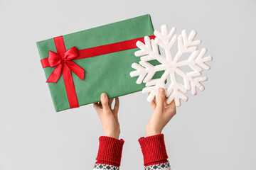 Hands holding Christmas gift and snowflake on grey background