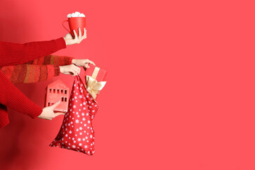 Hands holding Christmas gift bag and mug with marshmallows on red background