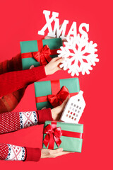 Hands holding gift boxes and Christmas decor on red background